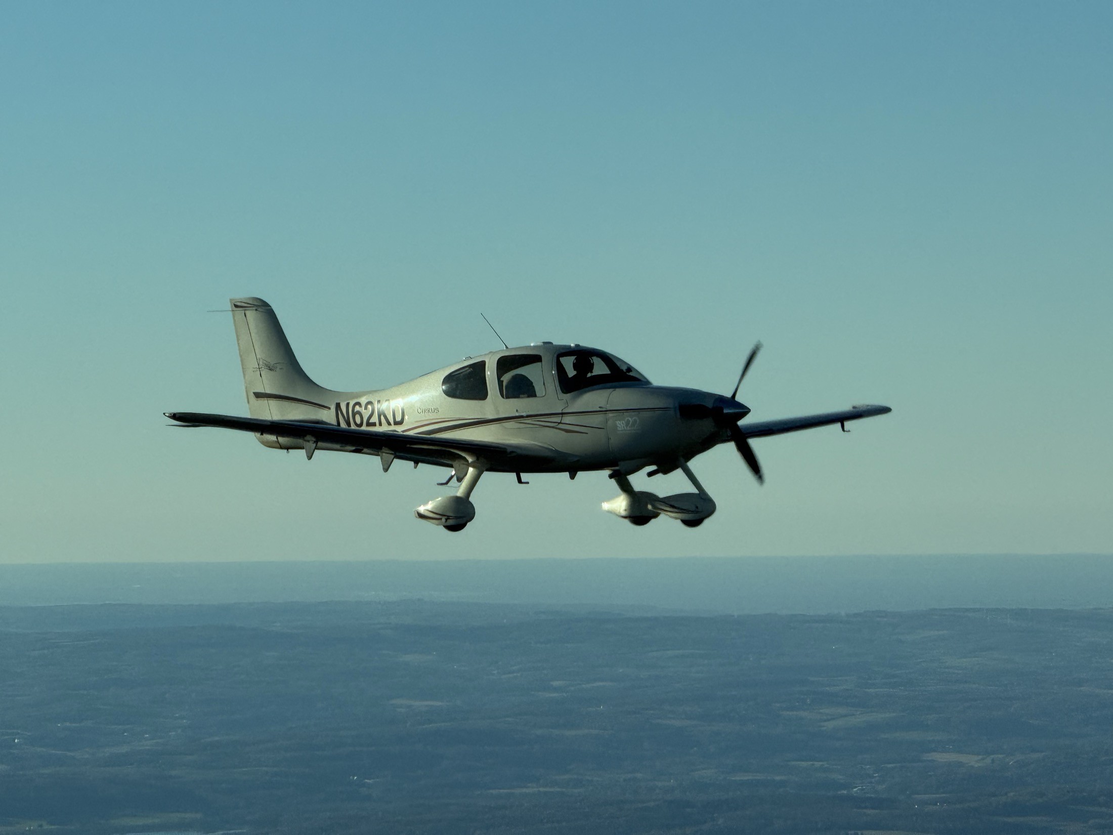 N62KD, a cream and taupe Cirrus SR22 Centennial Edition, flying above the hills.